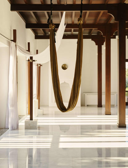 Aerial yoga swing suspended in a bright studio at Amanruya, with wooden beams and stone flooring.