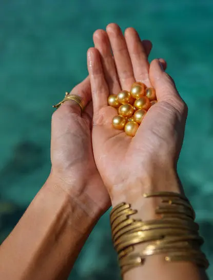 Hands holding golden pearls above turquoise water at Amanpulo.