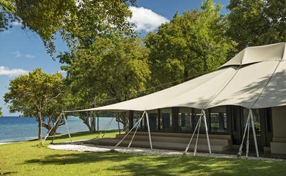 Amanwana's exterior view showing a modern pavilion with canvas canopy beneath tall trees overlooking the sea.