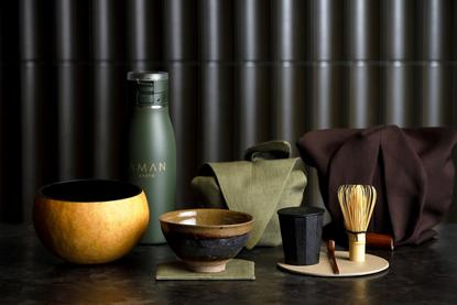 Aman Kyoto resort tea set with ceramic vessels, green tea, and traditional serving pieces arranged against a striped backdrop.