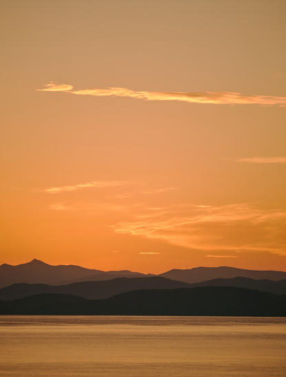 Sunset over calm waters with mountains silhouetted against an amber sky at Amanruya.