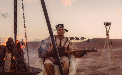 阿曼珍纳度假村，一位客人在日落时坐在船上眺望沙漠景观。