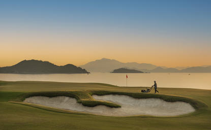 Amanoi golf course at sunset with coastal mountains and a water hazard in the foreground.