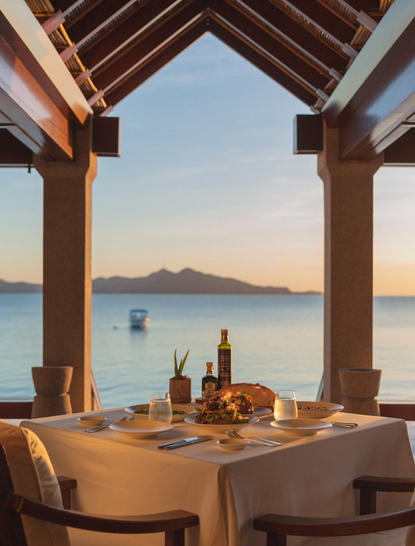 Tavolo da pranzo al tramonto presso la spiaggia di Amanpulo, con vista sul mare e montagne lontane.
