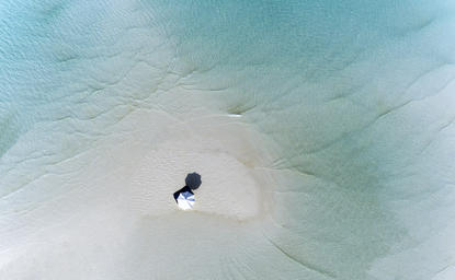 Aerial view of a solitary boat on white sand in shallow turquoise waters at Amanpulo resort.