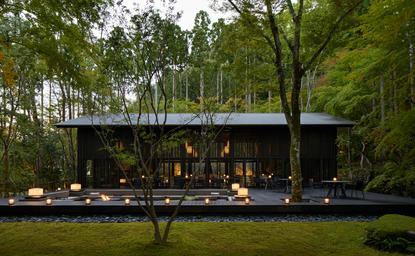 The Living Pavilion at Aman Kyoto resort, a modern black structure nestled beneath towering trees with illuminated interior and manicured lawn.