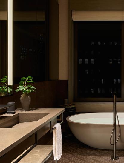 Suite salle de bains à l'Aman New York, avec baignoire blanche, vasque épurée et plantes vertes.
