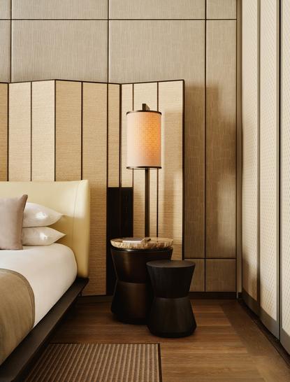 アマン ニューヨークのプレミアスイートの寝室。ベッドの横に黒いナイトテーブルとゴールドの照明が置かれている。