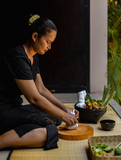Therapist preparing Khmer herbal compress at Amansara wellness workshop.