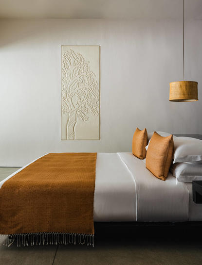 Principal bedroom at Amansara with wood-framed bed and ochre accents.