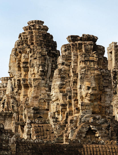 Stone faces of the Bayon temple at Amansara, Cambodia, carved into weathered sandstone towers.