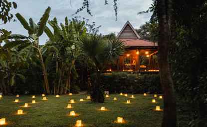 Candlelit pathway through gardens at Amansara at dusk, with illuminated pavilion beyond.