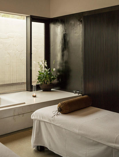 Spa treatment room at Amansara with massage table, dark accent wall, and walk-in shower.