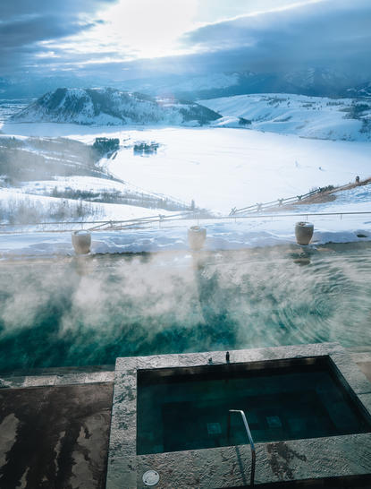 Aerial view of Amangani's plunge pool overlooking snow-covered mountains and misty valleys.