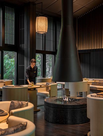 アマン京都のリビングパビリオン。中央の暖炉を囲み、木製家具が配置された開放的な空間。