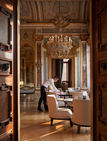 Ornate ballroom at Aman Venice with gilded wood panelling, crystal chandelier, and period furnishings.