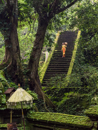 Stone steps lead through lush forest at Amandari, with a traditional umbrella shelter beside the path.