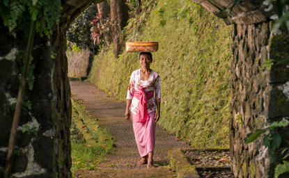 امرأة ترتدي ملابس وردية تسير عبر ممر حجري محاط بجدران مغطاة بالطحالب في منتجع أمانداري، إندونيسيا.