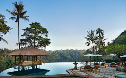 Amandari's clifftop pool overlooking verdant valley and river below, with wooden pavilion and loungers at dusk.