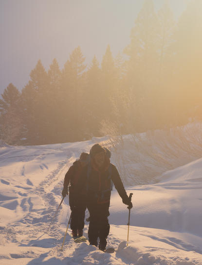 Solitary figure walking through snow-covered landscape at Amangani at sunrise, with forested peaks in mist.