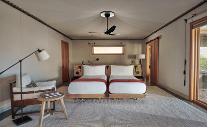 Twin bedroom at Amangiri with wooden headboard, bedside tables, and desert views through glass doors.