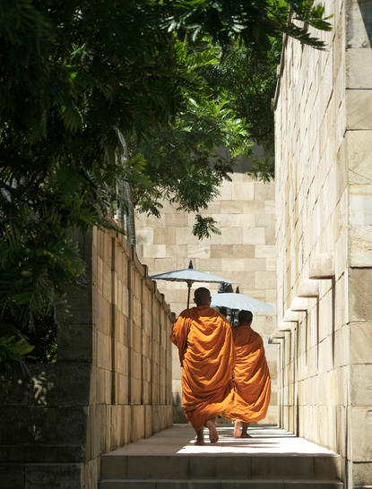 Buddhist monk in saffron robes walking through stone corridor at Amanjiwo, Central Java.