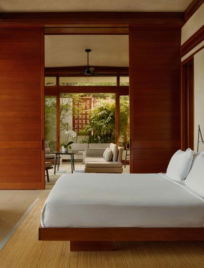 Chambre avec lit blanc et murs terracotta à Amanera, vue sur le jardin verdoyant par les portes vitrées.