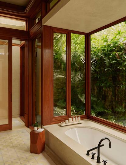 Salle de bains à Amanera avec baignoire, boiseries et baies vitrées sur la végétation.