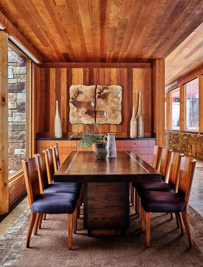 Wood-panelled dining room at Amangani with round table, mid-century chairs, and artwork on walls.
