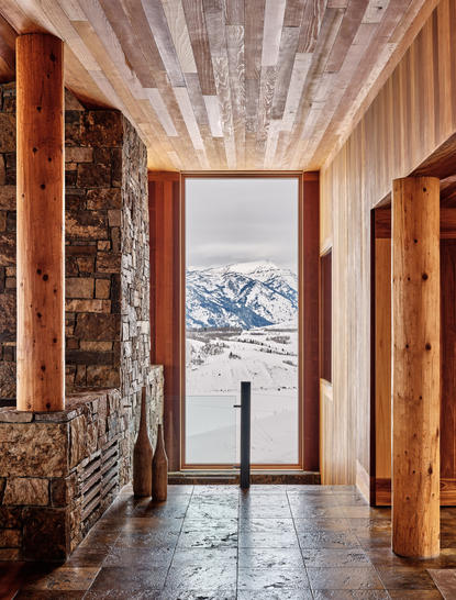 Corridor at Amangani with wooden doors, stone fireplace and snow-capped mountain vista through central doorway.