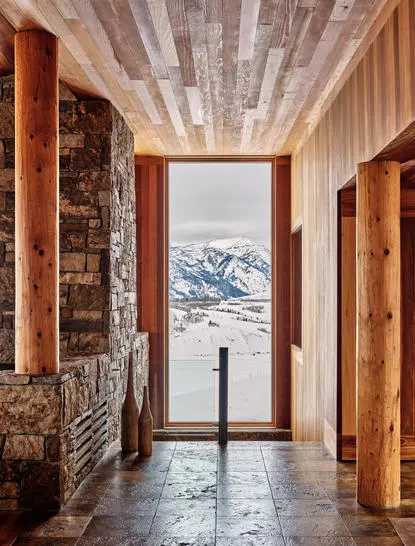 Corridor at Amangani with wooden doors, stone fireplace and snow-capped mountain vista through central doorway.