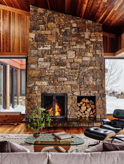 Amangani West Tatanka House interior with stacked-stone fireplace and wooden ceiling detail.