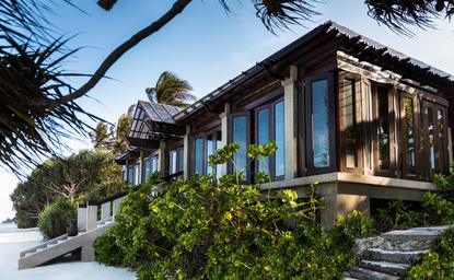 Nama exterior at Amanpulo resort, featuring dark timber architecture with verdant landscaping beneath clear sky.