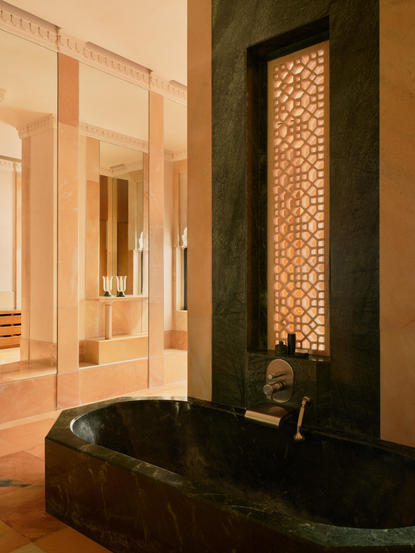Bathroom in Terrace Haveli Suite at Amanbagh with dark soaking tub and illuminated latticed window.