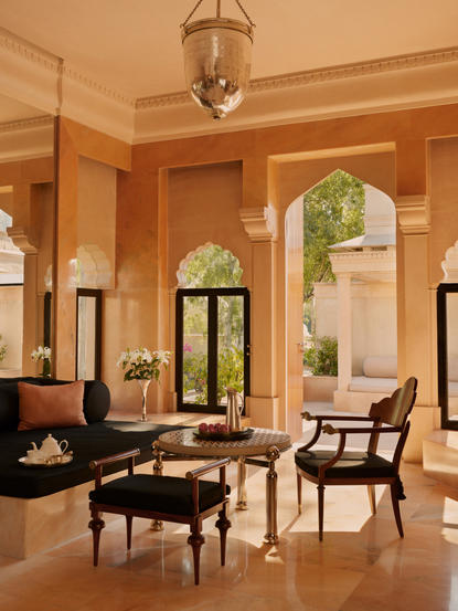 Terrace Haveli Suite living area at Amanbagh with warm ochre walls, traditional seating, and arched doorway opening to garden views.