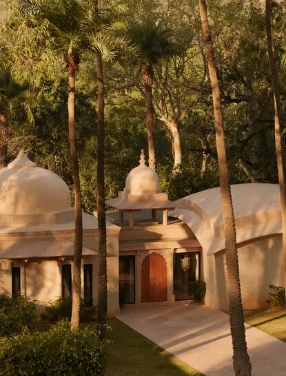 Pool Pavilion exterior at Amanbagh, India, at dusk with illuminated architecture amongst tall trees.