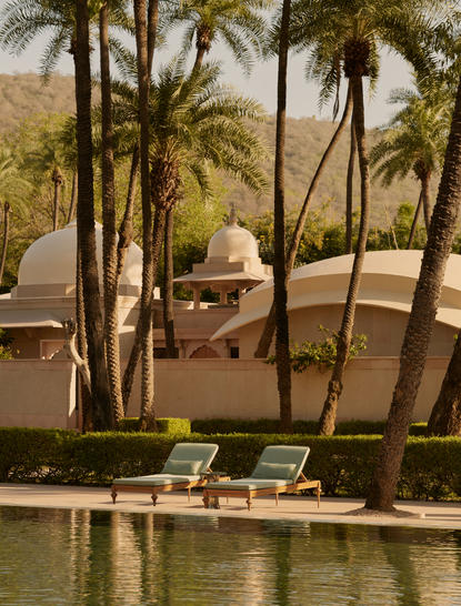 Sunlit plunge pool at Amanbagh with loungers and palm trees overlooking the Rajasthan landscape.