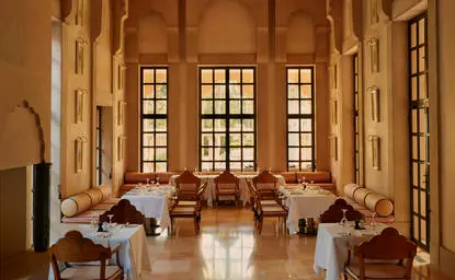 Amanbagh restaurant with tall arched windows, wooden chairs, and warm terracotta tones.
