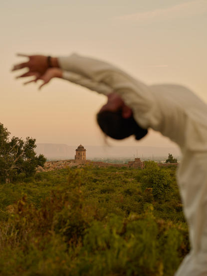 Yoga practice at Amanbagh, with a guest in a forward bend pose overlooking green gardens at dawn.