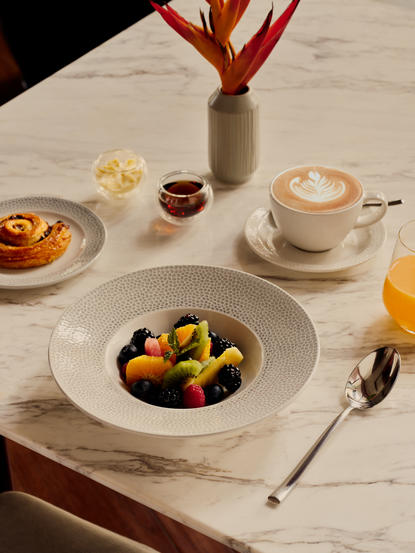 Petit-déjeuner à Amanera : assiettes de fruits frais et pâtisseries sur marbre blanc, avec café.