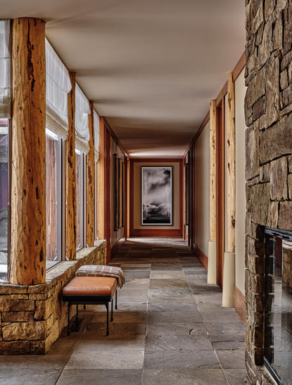 Corridor at Amangani with stone walls, wooden framed windows and a bench, leading towards artwork.