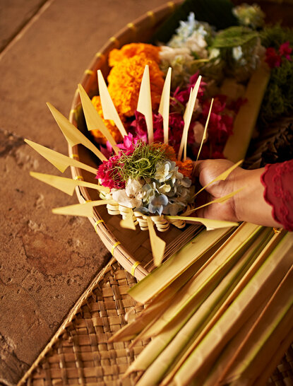 Amandari রিসোর্টে ফুলের অর্ঘ্য প্রস্তুতি, সোনালি ঝুড়িতে রাখা রঙিন ফুল এবং সবুজ পাতা।