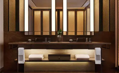 Salle de bains de la suite deluxe, Aman New York, avec vasque intégrée et miroir éclairé.