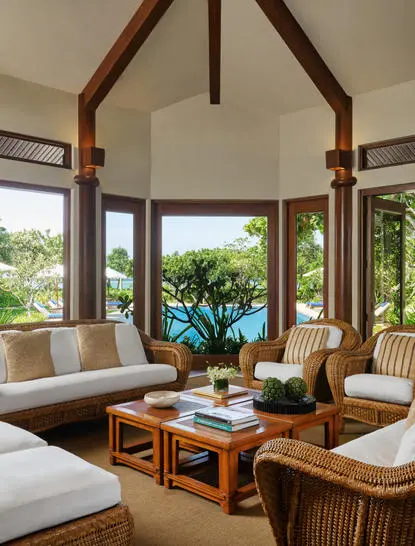Sala de estar de cuatro dormitorios en Amanpulo resort, con vigas de madera, sofás claros y vistas al jardín tropical.