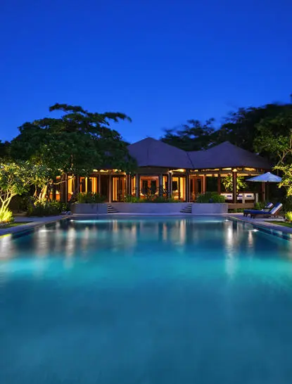 Piscina iluminada al atardecer en el resort Amanpulo, Filipinas, reflejando luces cálidas en sus aguas turquesas.