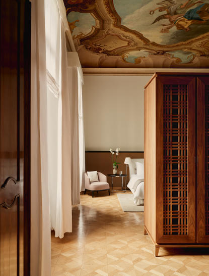 Bedroom at Aman Venice with view through open doorway to bed and traditional Venetian ceiling fresco.