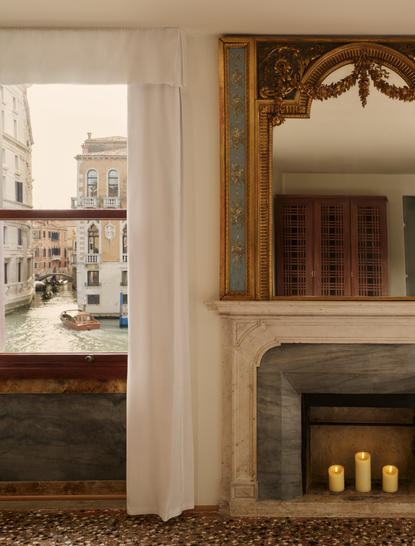 Grand Canal Suite bedroom at Aman Venice, featuring a fireplace with candles and doorway to adjoining room.