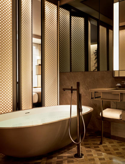 Bathroom in a Premier Suite at Aman New York featuring a freestanding soaking tub with floor-mounted filler, illuminated wooden screens, and warm lighting.