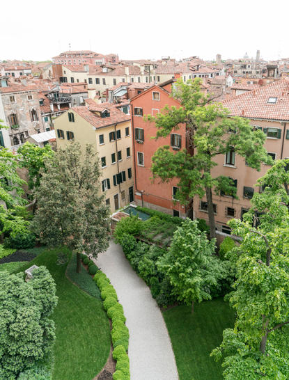 Entrance garden at Aman Venice hotel, with verdant grounds and terracotta buildings overlooking a Venetian canal.