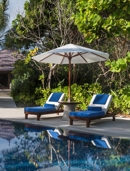 Two blue sun loungers and striped parasol beside a pool at Amanpulo, framed by tropical greenery.